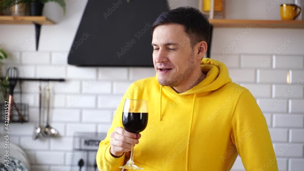 Relaxed young man drinks red wine, standing at kitchen table. Adult guy resting with alcohol in kitchen. Relaxed young man drinks red wine, standing at kitchen table. Adult guy resting with alcohol in kitchen.