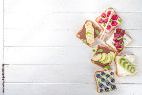 Healthy fruit and berry sandwiches. Tasty diet toast bread with cream cheese and banana, apple, raspberry, blueberry, strawberry, top view copy space