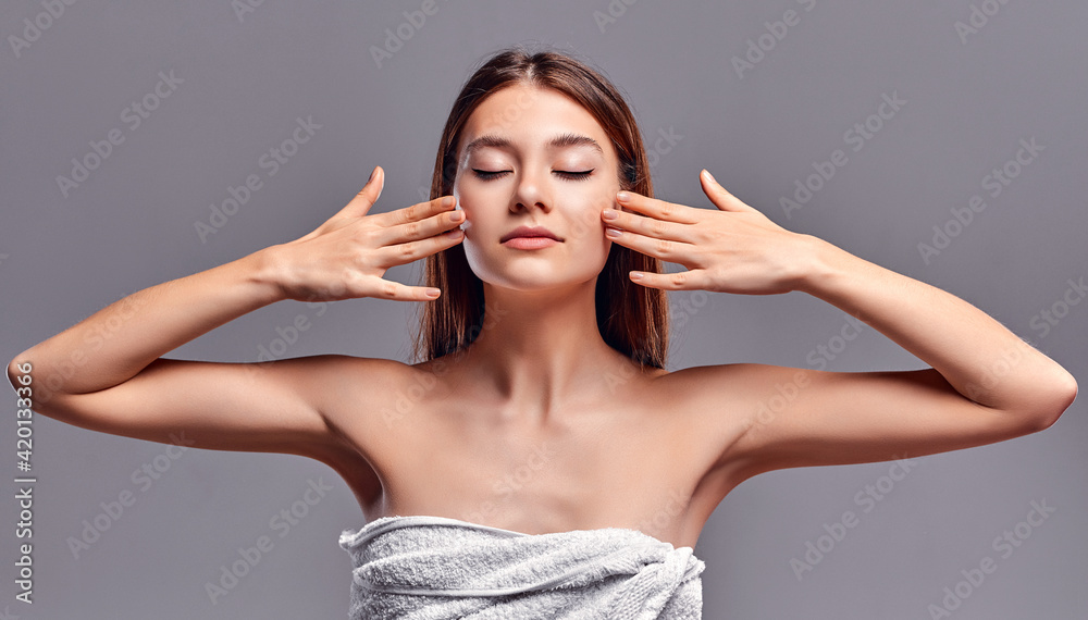 Fototapeta premium Beautiful young woman with clean perfect skin. Portrait of beauty model with natural nude makeup. Spa, skin care and wellness. Close up, gray background, copyspace.