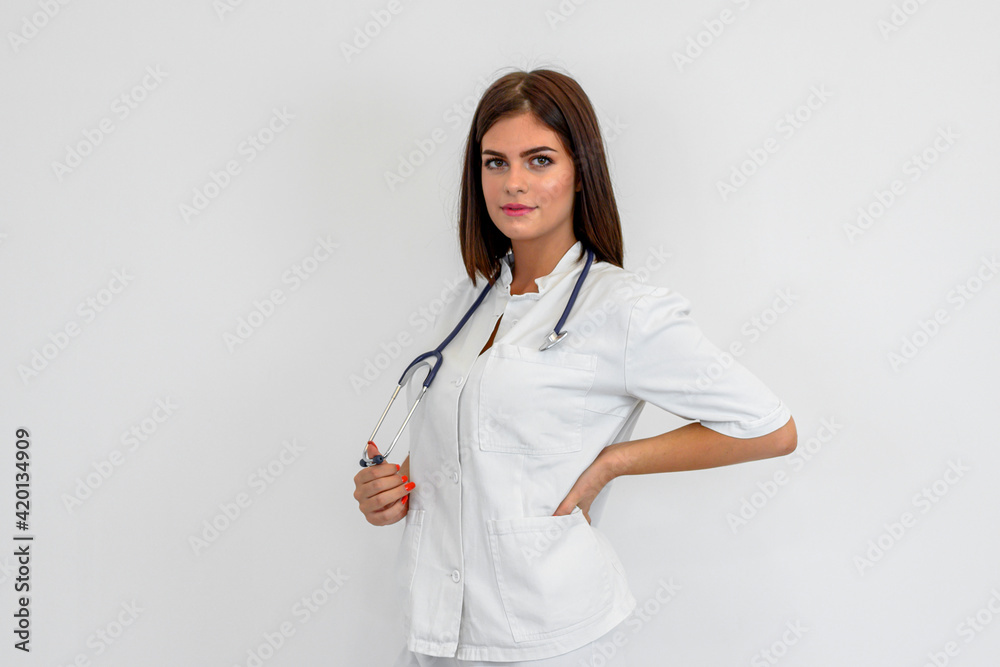 Portrait of young brunette woman in uniform. She is holding stethoscope around neck. White background. Portrait of young brunette woman in uniform. She is holding stethoscope around neck. White background.