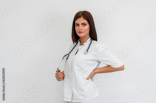 Portrait of young brunette woman in uniform. She is holding stethoscope around neck. White background.