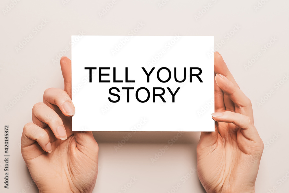 Female hands hold card paper with text Tell Your Story on a yellow background. Business and finance concept Female hands hold card paper with text Tell Your Story on a yellow background. Business and finance concept