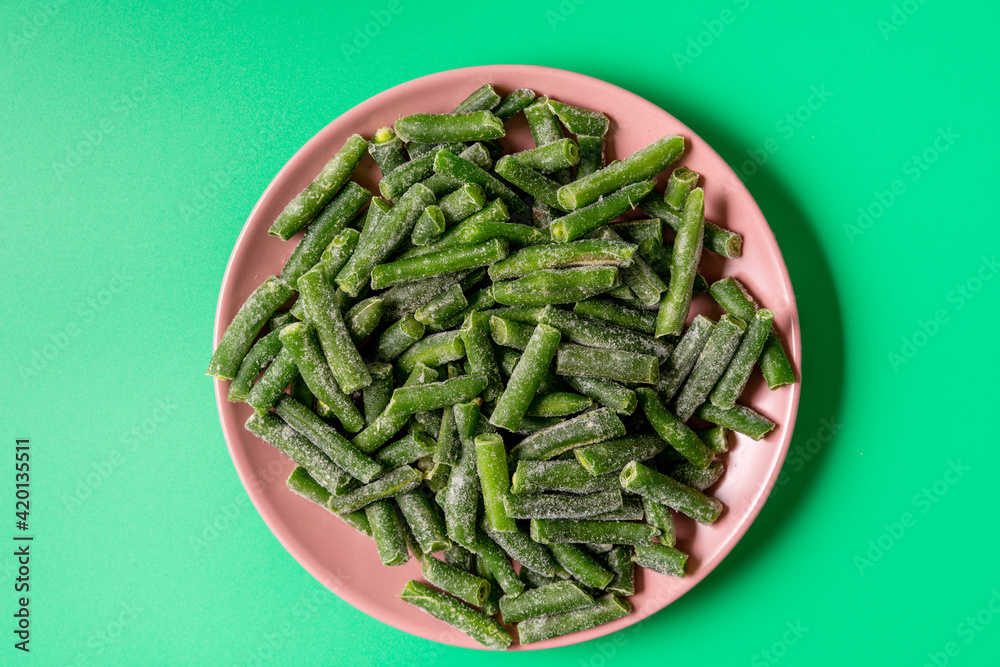 Frozen green string beans in a plate on green background. Frozen green string beans in a plate on green background.