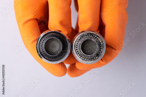 Gloved hands hold two faucet nozzles in water-corroded and cleaned.