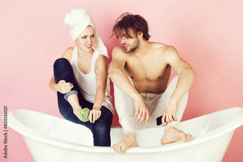Obraz premium Funny couple in love sitting on white bathtub on pink background, family, relationship and romance, spa and beauty, relax and hygiene.