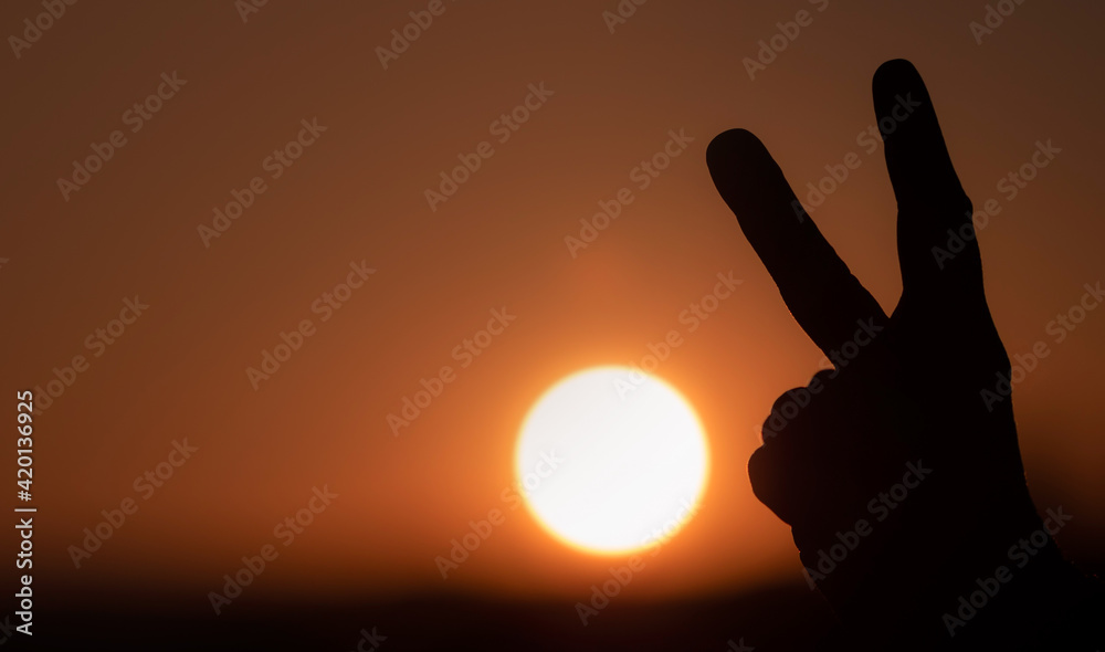 hand silhouette showing peace sign in sunrise