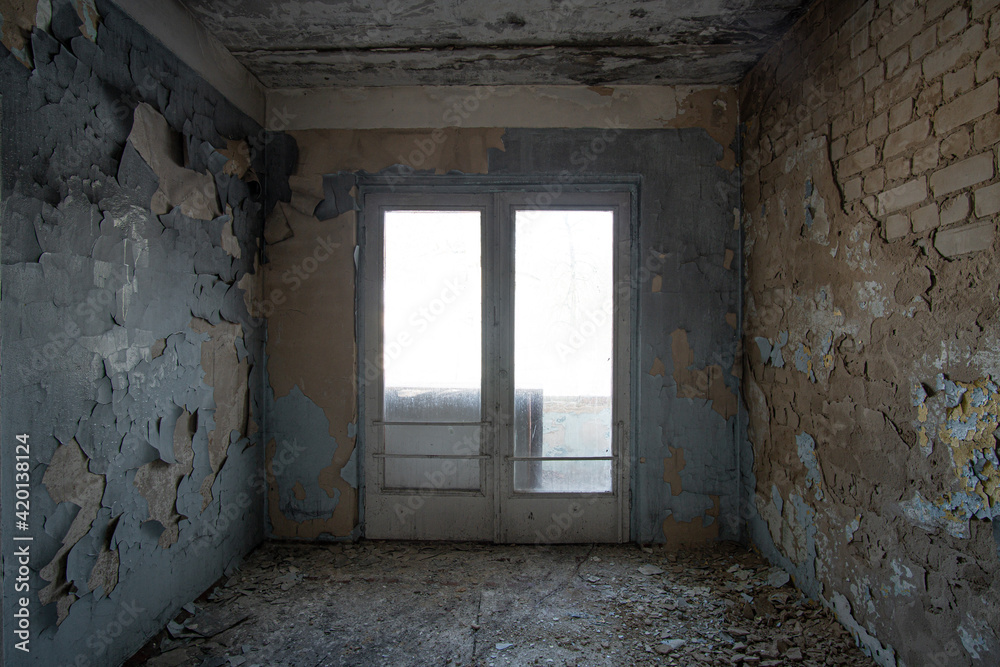 Interior of an abandoned concrete building with a window in the center and peeling paint on the walls.