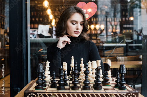 Beautiful girl play chess, queen’s gambit play and everyone wins, smart and pensive face. White and black chess pieces are displayed on the board. Mental game, lot of time to last, not for fools.