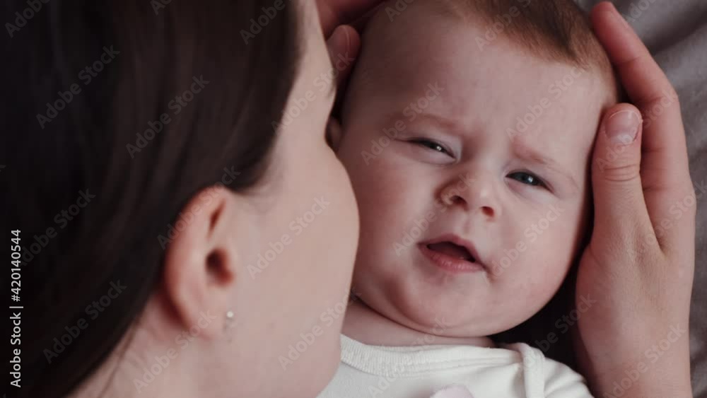 Close-up top view of loving young mother is playing with her newborn baby in nursery lying on comfortable bed at home. Concept of children, baby, parenthood, childhood, life, maternity, motherhood Close-up top view of loving young mother is playing with her newborn baby in nursery lying on comfortable bed at home. Concept of children, baby, parenthood, childhood, life, maternity, motherhood