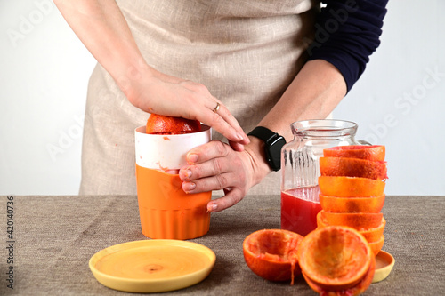 The woman squeezes the juice out of the oranges with her right hand.
