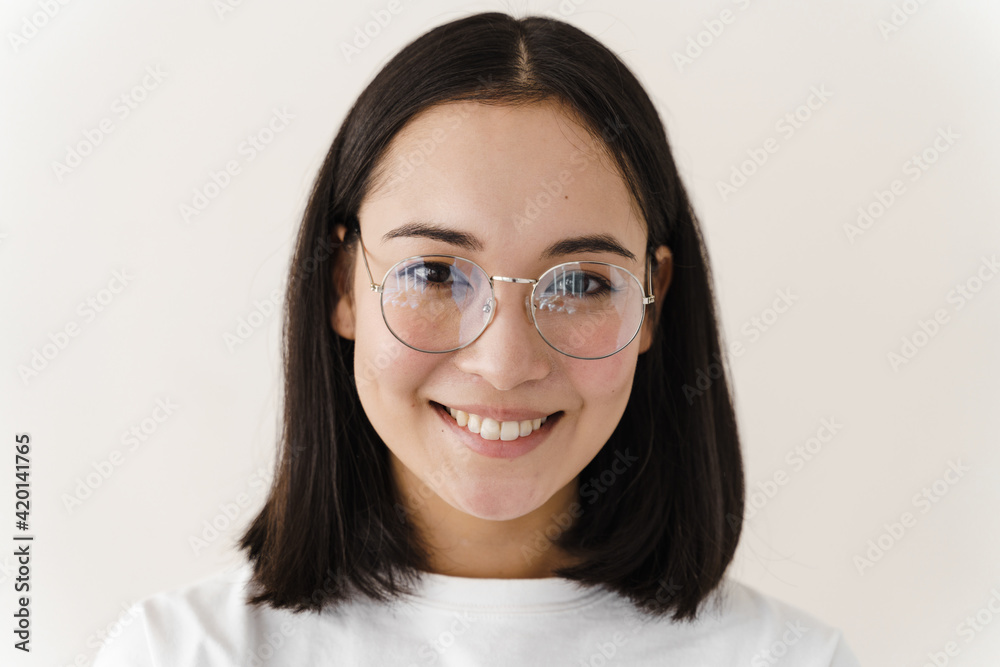 Attractive girl with glasses looks straight into the camera. Young woman posing on a white wall background. Attractive girl with glasses looks straight into the camera. Young woman posing on a white wall background.