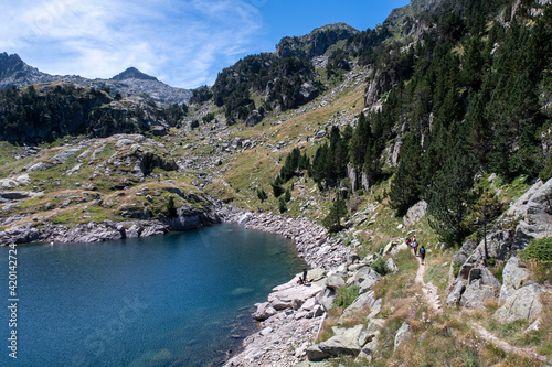 group of excursionists seen from far away walking on a footpath around a high-mountain glacier lake in Aiguestortes national park, Lleida, Spain