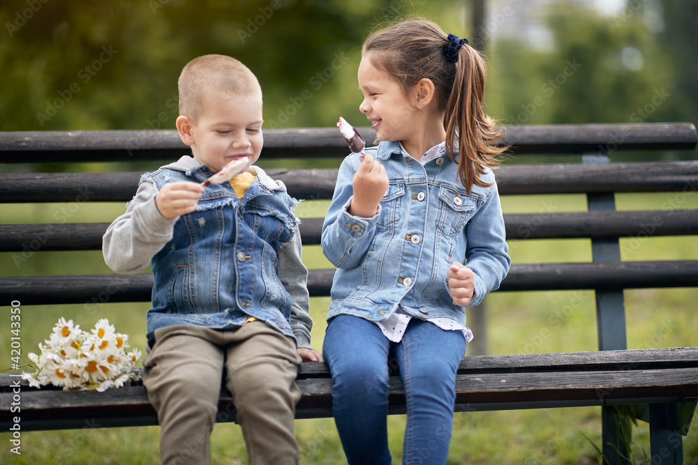 boy and a girl sitting on a bench in park, eating ice cream, talking ...