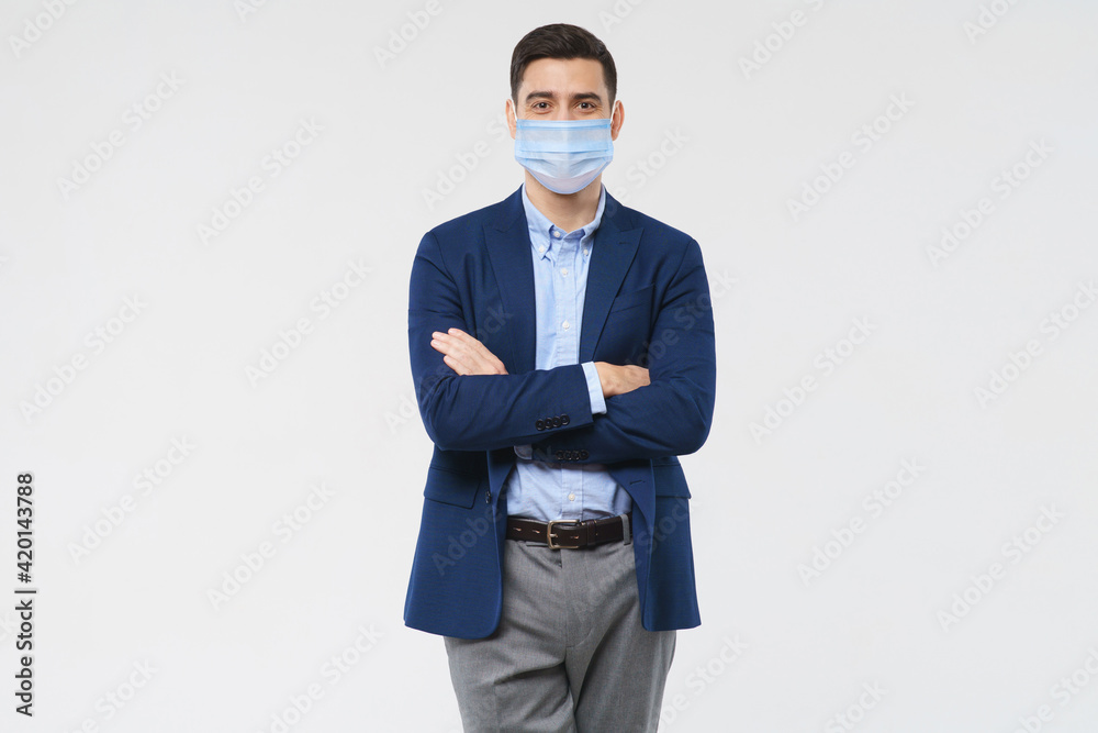 Young business man wearing medical mask, standing with crossed arms isolated on gray background Young business man wearing medical mask, standing with crossed arms isolated on gray background