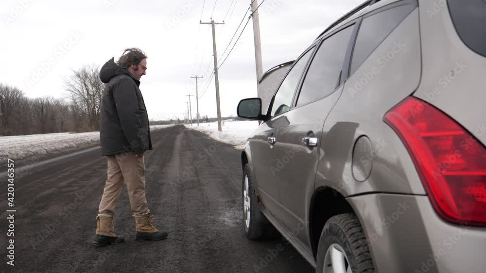 Man kicking his car tire off the frustration that broke down on the side of the road during winter Man kicking his car tire off the frustration that broke down on the side of the road during winter