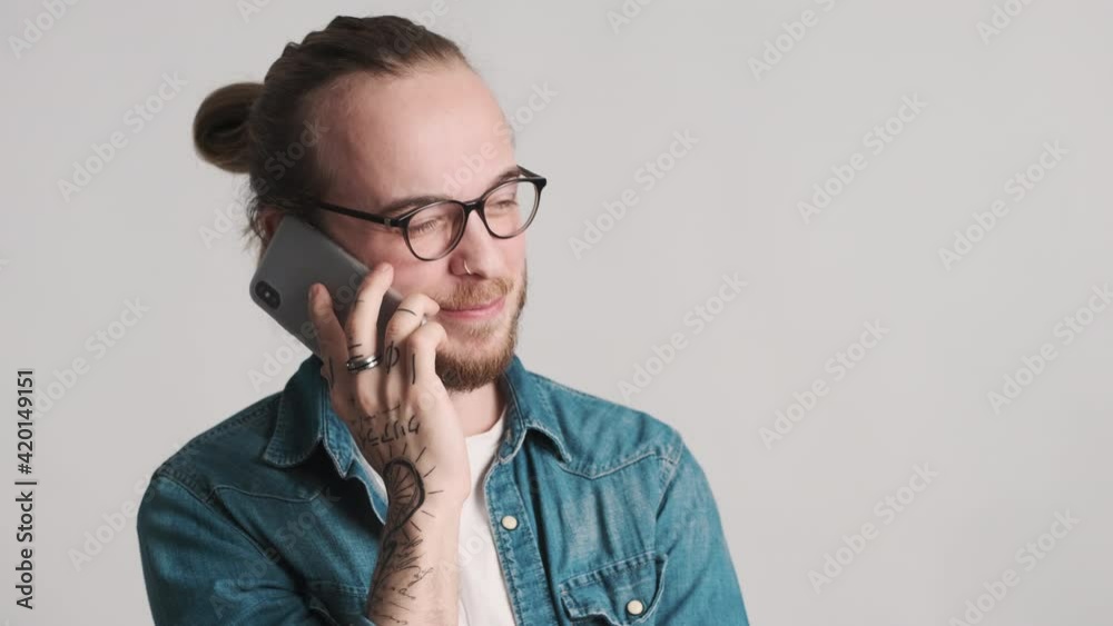 Young bearded man in eyeglasses dressed in casual wear looking happy talking with friend on phone over white background. Always in touch Young bearded man in eyeglasses dressed in casual wear looking happy talking with friend on phone over white background. Always in touch
