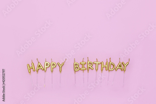 Happy Birthday words are made of golden candles on pastel pink background. Minimal birthday concept. Copy space, flat lay. Greeting card template. Festive banner.