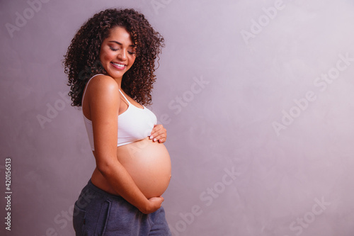 Beautiful pregnant Afro woman, posing for photo showing her pregnancy belly, smiling for the photo and for life, in an essay done in studio to contemplate the beauty of motherhood