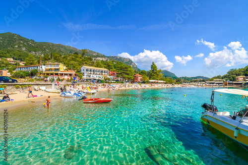 Tourists relax in the clear waters and on the sandy Palaiokastritsa beach on the Aegean island of Corfu, Greece.