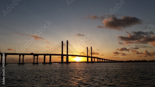 Nascer do sol por trás de uma ponte que atravessa um rio.