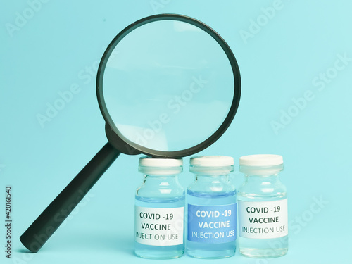 Selective focus COVID 19 VACCINES variant with magnifying glass isolated on blue background.   photo