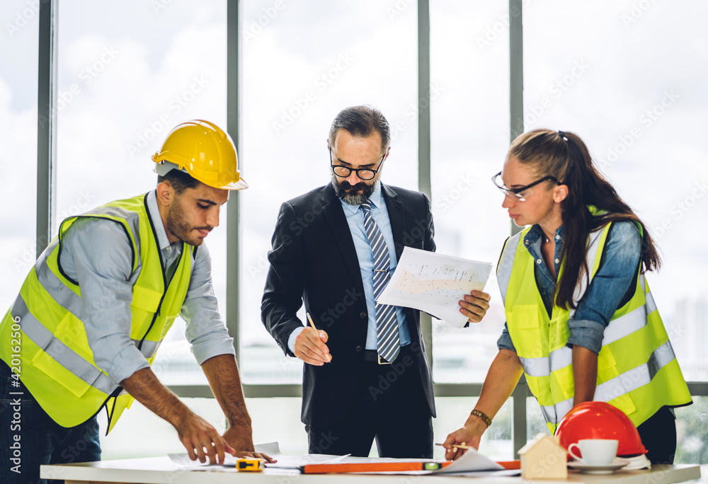 Professional of team engineers cargo foreman in helmets working with blueprint and construction tools on table at the construction site