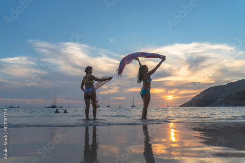 Two woman poses with a beautiful sarong on the beach during the COVID-19 outbreak not many tourists on Nai Harn beach. but still have local people on the Nai Harn beach Phuket Thailand..