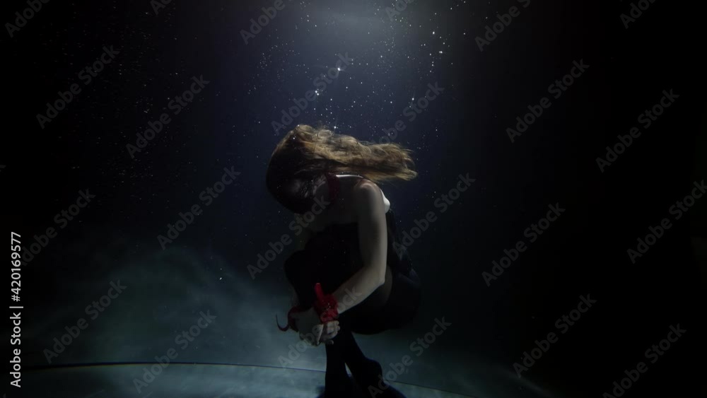 mysterious woman on bottom of pool in darkness, floating and swimming in beam of light, slow motion