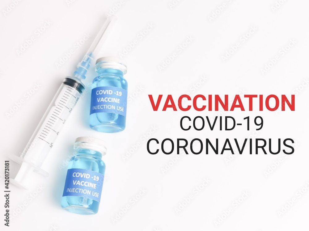 Phrase VACCINATION COVID 19 CORONAVIRUS written on white background with two bottles vaccine and syringe. Phrase VACCINATION COVID 19 CORONAVIRUS written on white background with two bottles vaccine and syringe.