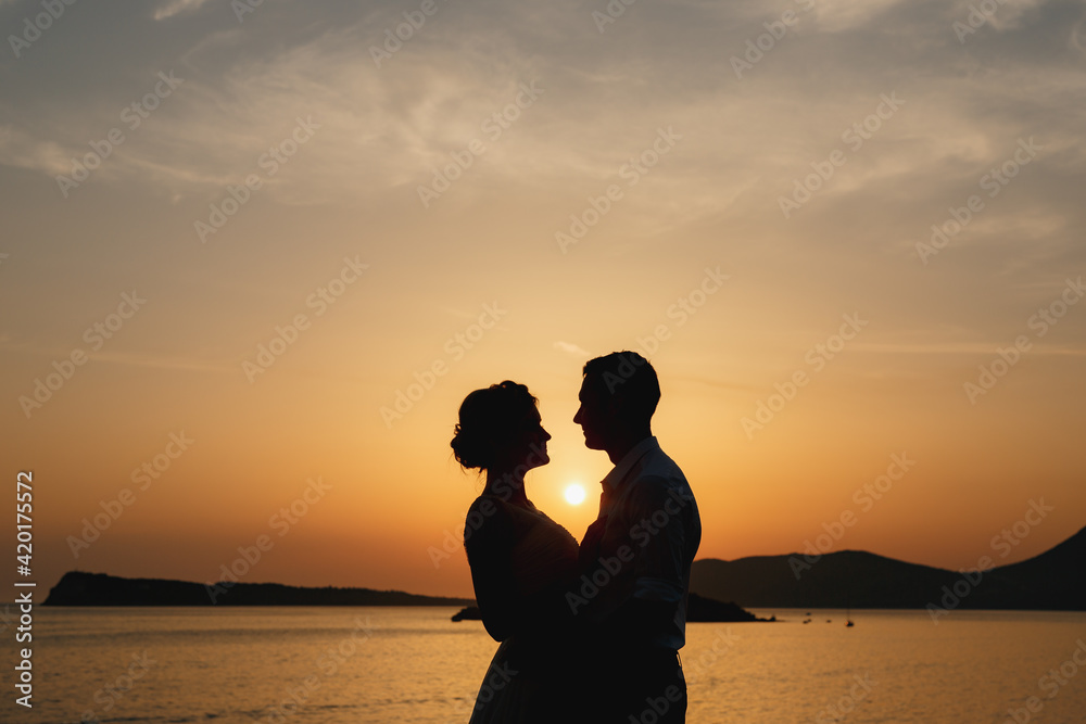 The bride and groom are embracing on the seashore at sunset and look at each other 