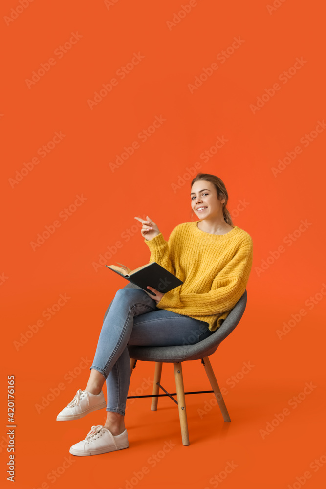 Beautiful young woman reading book while sitting in armchair on color background Beautiful young woman reading book while sitting in armchair on color background