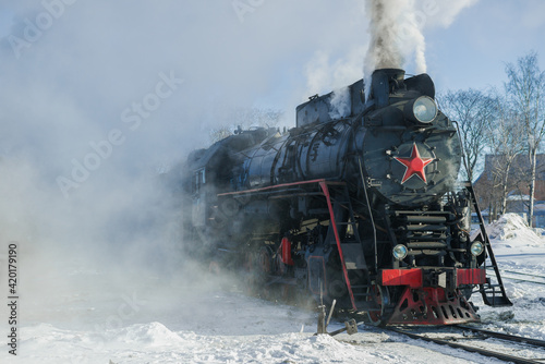 Old freight steam locomotive in the clouds of steam on a frosty day. Russia