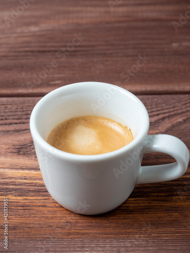 a white cup with a delicious and aromatic espresso on a wooden background. Vertical photo, side view