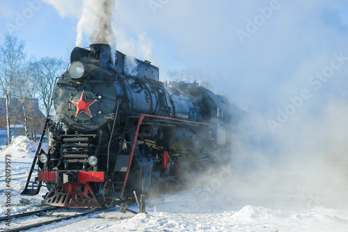 Old Soviet steam locomotive in the clouds of steam on a frosty winter day. Russia