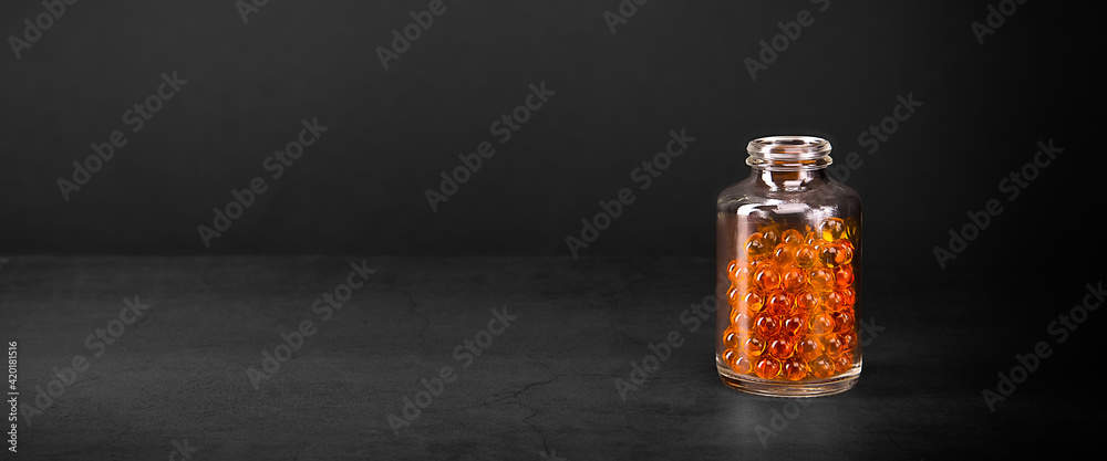 A glass jar with pills of bright orange yellow color on a gray background. A glass jar with pills of bright orange yellow color on a gray background.