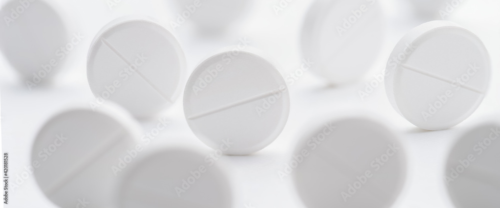 A pile of white pills scattered on a bright white background. Selective focus.