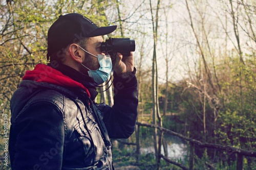 Middle age man observing in the nature wearing a surgical mask , concept of bird watching during Corona Virus