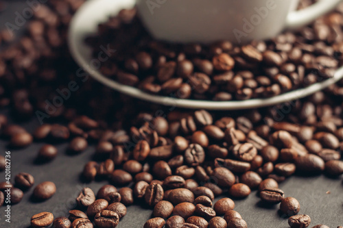 saucer with coffee beans and white cup on gray table close-up