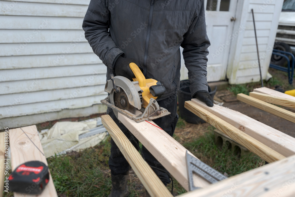 Closeup of a carpenter cutting a wood plank with a chainsaw.
