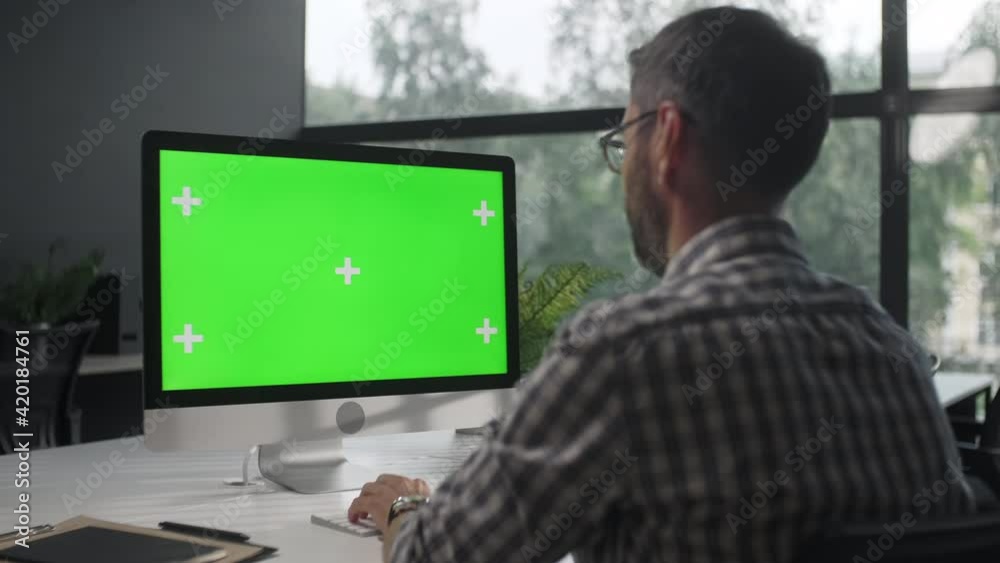 Over The Shoulder Shot Of a Business Man Working In Office Interior On Pc On Desk, Looking At Display Green Screen. Office Person Using Computer With Computer Green Screen, Sitting at Table. Over The Shoulder Shot Of a Business Man Working In Office Interior On Pc On Desk, Looking At Display Green Screen. Office Person Using Computer With Computer Green Screen, Sitting at Table.