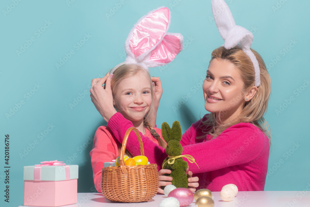 Mother and child daughter celebrating Easter. Cute little girl with funny face in bunny ears laughing, smiling and having fun isolated on blue.