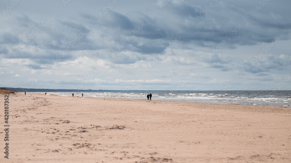 View of the seashore and people walking in a cloudy stormy day. 16x9
