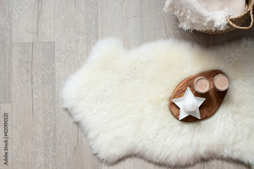 A mug of coffee, cocoa on a wooden board with candles. On the floor is a sheep skin, a wicker basket with a blanket.