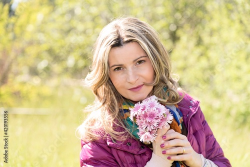 Ritratto di donna bionda immersa nel verde con in mano un mazzo di fiori di campo.