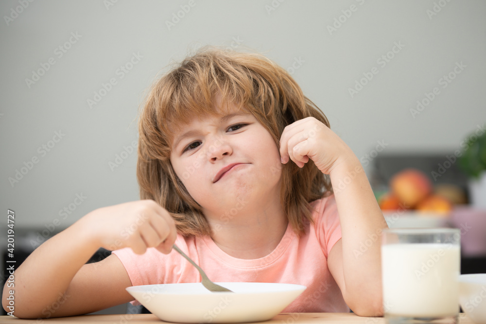 Child eating healthy food at home. Unhappy Caucasian child sit at table at home kitchen have no appetite. Upset little kid refuse to eat organic cereals with milk. Child eating healthy food at home. Unhappy Caucasian child sit at table at home kitchen have no appetite. Upset little kid refuse to eat organic cereals with milk.