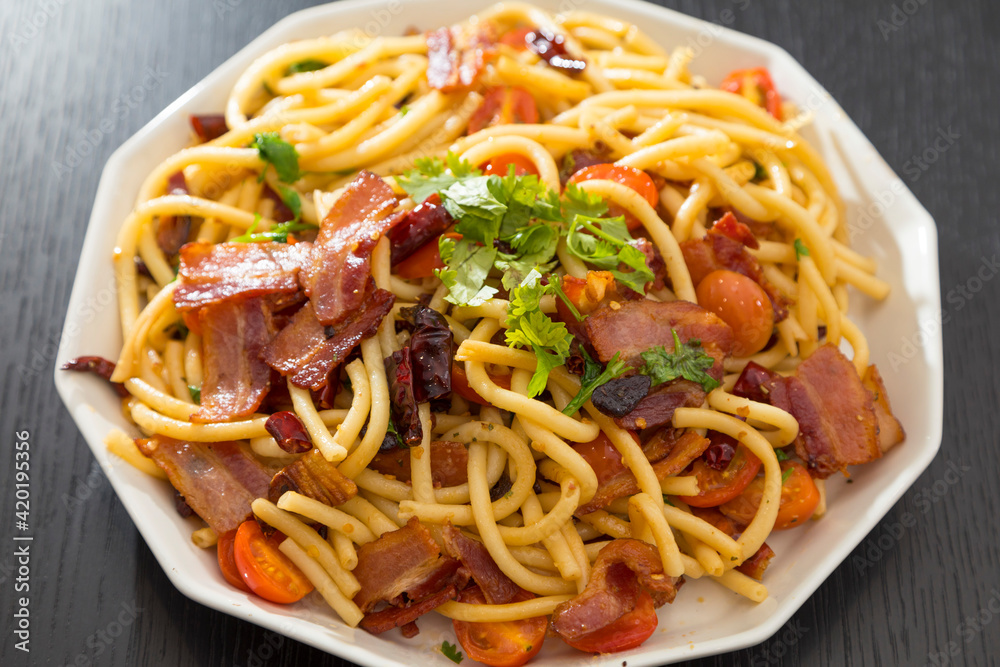 Spaghetti alla Amatriciana with bacon, tomatoes and dried chili on black wood table.