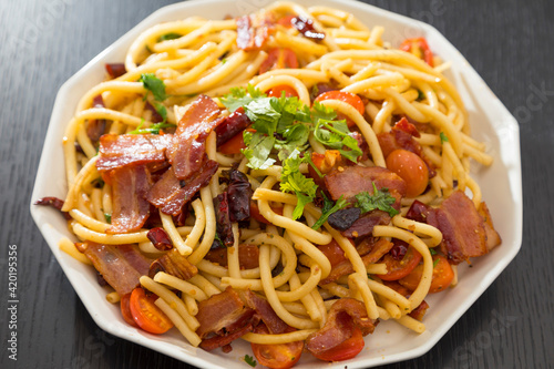 Spaghetti alla Amatriciana with bacon, tomatoes and dried chili on black wood table.