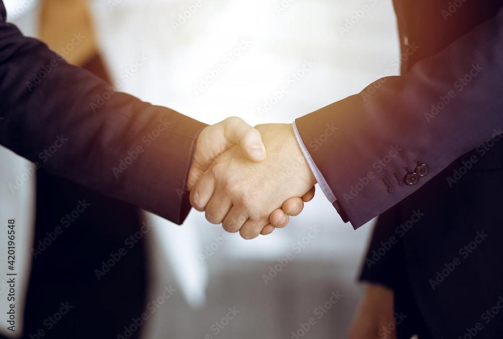 Unknown businesspeople are shaking their hands after signing a contract, while standing together in a sunny modern office, close-up. Business communication concept Unknown businesspeople are shaking their hands after signing a contract, while standing together in a sunny modern office, close-up. Business communication concept