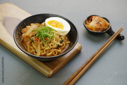 Ramyeon or Korean instant noodle with Kimchi on black bowl. Isolated in gray background, wooden board and chopstick