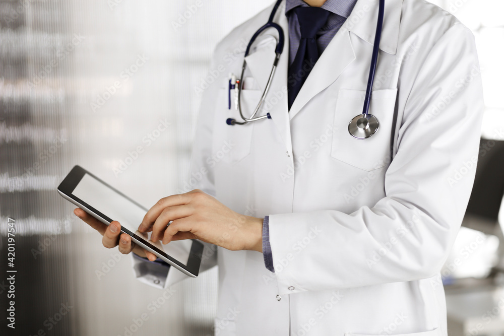 Unknown male doctor using tablet computer in clinic near his working place, closeup. Perfect medical service in hospital. Medicine and healthcare concept Unknown male doctor using tablet computer in clinic near his working place, closeup. Perfect medical service in hospital. Medicine and healthcare concept